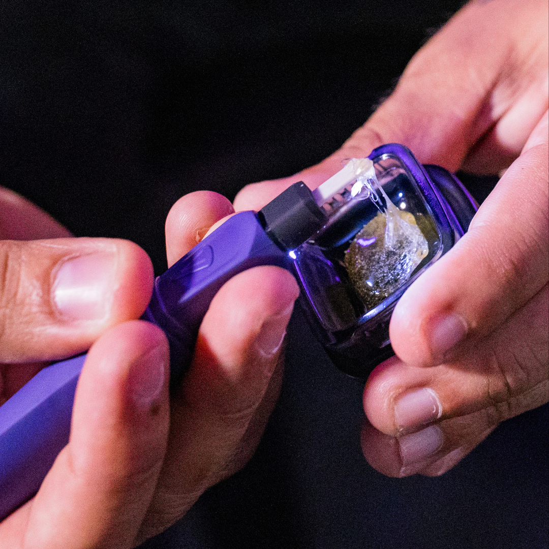 Lifestyle photography of a user loading concentrate into an AERIS portable dab rig using the Focus V SABER electric dab tool hot knife during an outdoor session
